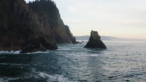 Low-flight-between-rocky-spire-rising-from-Pacific-Ocean-and-Oregon-Coast-cliff