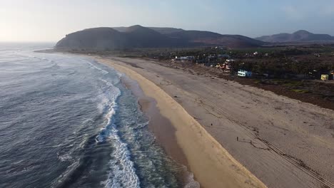 La-Gente-Camina-Por-La-Playa-Al-Atardecer-Mientras-Las-Olas-Rompen-Contra-La-Costa-Arenosa-Con-Montañas-Cerca-De-El-Pescadero.