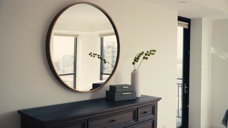 a-circular-mirror,-black-dresser,-and-modern-decorations-in-a-bedroom-of-a-home