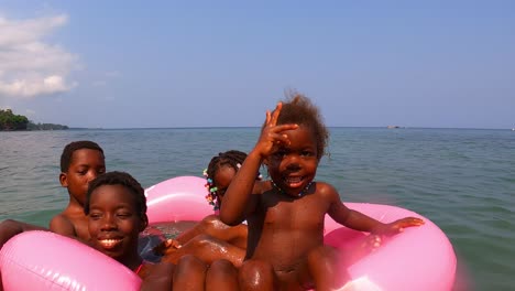 African-children-smiling-and-playing-on-a-float-at-sea-of-a-beach-in-Sao-Tome,Africa