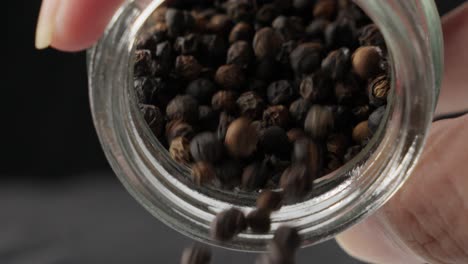 Person-Pouring-Dried-Whole-Black-Peppercorns