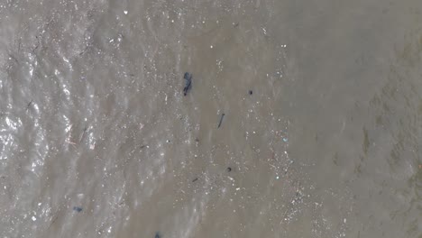 Slow-motion-low-altitude-top-down-drone-shot-of-polluted-ocean-filled-with-floating-trash-and-debris-and-muddy-sewage-runoff-in-Bali-Indonesia