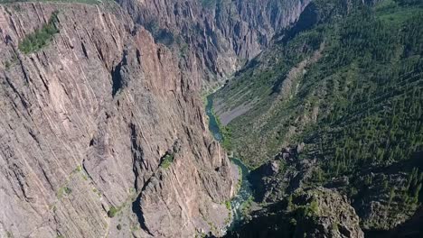 A-fly-over-drone-shot-panning-down-into-Black-Canyon,-an-extreme,-steep-walled-gorge,-containing-massive-rock-spires,-carved-out-by-the-Gunnison-River,-in-Gunnison-National-Park,-in-Western-Colorado