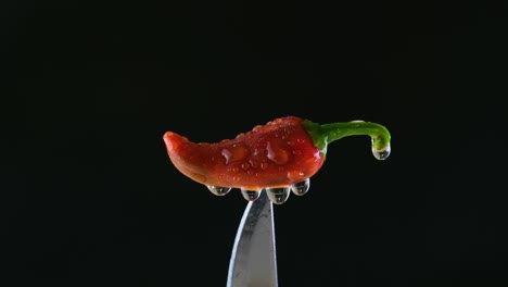 Spicy-red-Jalapeno-chilli-pepper-dripping-wet-on-sharp-knife-with-water-spray-against-black-background