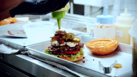 4K-Cinematic-food-cooking-footage-of-a-chef-preparing-and-making-a-delicious-homemade-burger-in-a-restaurant-kitchen-in-slow-motion-putting-the-sauce-on-top-of-the-smashed-burger