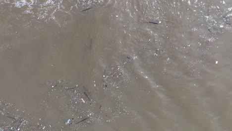 Rotating-top-down-drone-shot-of-polluted-water-filled-with-floating-trash-and-muddy-river-runoff-mixing-with-turqouise-tropical-water-of-Bali-Indonesia