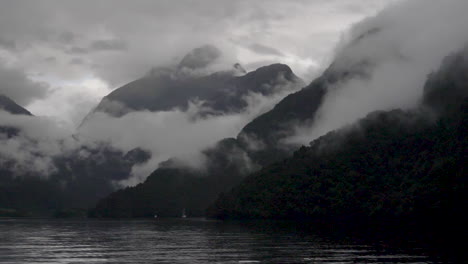 Slow-motion-static-footage-of-misty-and-cloudy-mountains-in-Doubtful-Sound-with-water-in-foreground---Patea,-New-Zealand