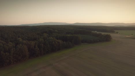 Espectacular-Y-épica-Toma-De-Drones-De-Los-Bosques-Y-Campos-Con-Montañas-En-El-Fondo,-Vista-De-Pájaro,-Durante-Una-Puesta-De-Sol-O-Un-Amanecer-Al-Atardecer-O-Al-Amanecer