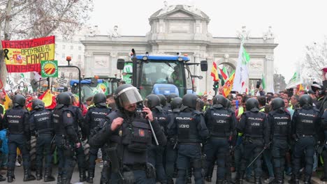 Zoom-out-view-of-police-officers-stand-guard-as-Spanish-farmers-and-agricultural-unions-gather-at-Plaza-de-la-Independencia-to-protest-against-unfair-competition,-agricultural-and-government-policies