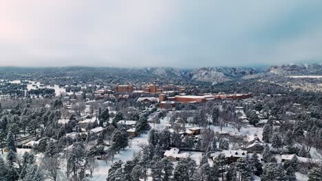 Panoramic-aerial-parallax-over-snow-covered-evergreen-forest-as-striking-brown-hotel-stands-out-in-Rocky-Mountains
