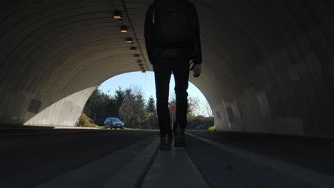 Backlit-silhouette-of-a-person-walking-in-a-tunnel,-car-approaching-in-the-background,-daylight