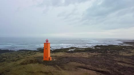 Orange-lighthouse-stands-in-contrast-against-a-rocky,-moody-coastline-in-Iceland