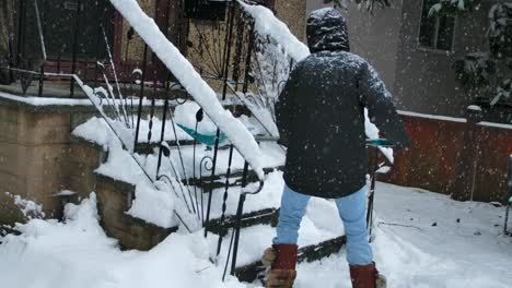 Man-sweeping-snow-from-stairs-near-house-in-winter