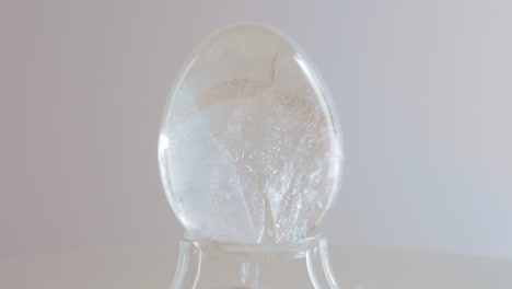 Klares-Quarzkristall-Mineral-Ei,-Das-Auf-Einem-Drehtisch-Vor-Einem-Weißen-Hintergrund-Rotiert