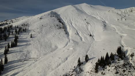 Snow-covered-Lespezi-Peak-in-the-Fagaras-Mountains-with-conifers,-under-a-clear-blue-sky,-aerial-view