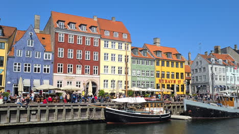 Copenhague,-Dinamarca,-El-Distrito-De-Nyhavn,-Coloridos-Edificios-Frente-Al-Mar,-Barcos-Y-Personas-En-El-Paseo-Marítimo