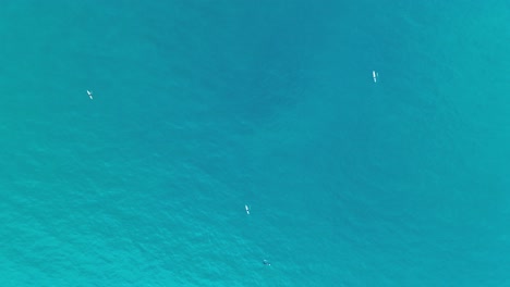 High-altitude-top-down-drone-shot-of-unrecognizeable-traditional-fishermen-in-traditional-boats-in-turquoise-tropical-water-in-Bali-Indonesia