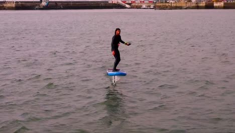 Man-Hydrofoil-Surfing-in-Lisbon-Harbor,-Drone-shot