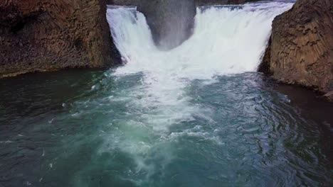 Static-aerial-of-twin-waterfalls-flowing-into-a-dark-blue-pond-in-Iceland