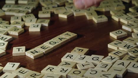 Die-Finger-Der-Rechten-Hand-Bewegen-Scrabble-Steine-Auf-Dem-Tisch,-Um-Ein-Negatives-Wort-Zu-Bilden