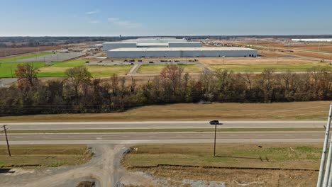 Aerial-following-vehicle-driving-past-Ford's-BlueOval-City,-showcasing-the-facilities'-construction-progress-in-the-background