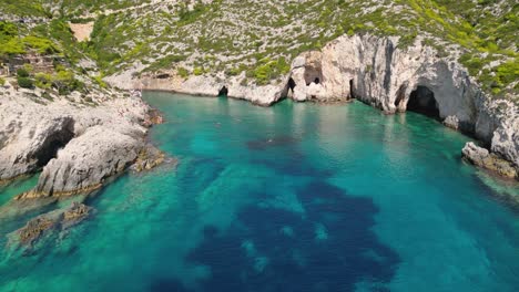 Rocky-coastline-with-people-swimming-in-blue-water