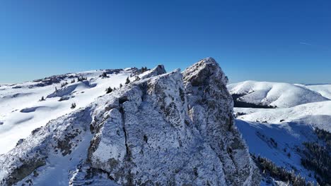 Snow-covered-Coltii-Strungii-peak-under-a-clear-blue-sky,-Bucegi-Mountains,-aerial-view
