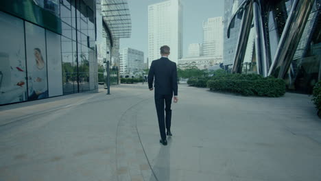 View-From-Behind-Of-Man-In-Black-Suit-Walking-Outside-Then-Happy-Jumping,-Cinematic-Tracking-Shot