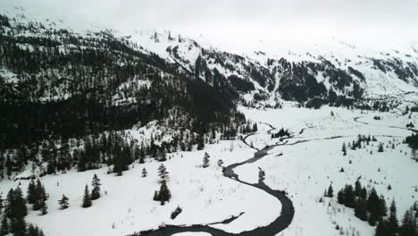 Drone-Inclinándose-Sobre-Un-Pequeño-Río-En-Un-Paisaje-Montañoso-En-La-Nieve-De-Alaska