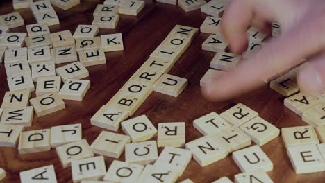 Hand-forms-words-ABORTION-and-RULE-in-crossword-Scrabble-tile-letters