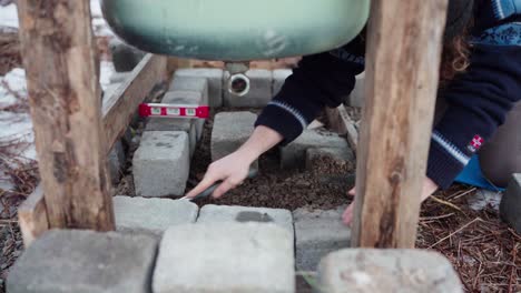 The-Man-is-Compressing-the-Concrete-Block-and-then-Employing-a-Level-to-Align-it-Beneath-the-DIY-Hot-Tub---Close-Up