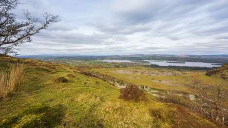 Panorama-motion-timelapse-of-rural-nature-farmland-with-trees-in-the-foreground-grass-field-and-hills-and-lake-in-distance-during-cloudy-day-viewed-from-Carrowkeel-in-county-Sligo-in-Ireland