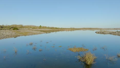 Slow-aerial-dolly-over-shrub-branches-in-shallow-flood-water-reflecting-blue-sky-on-sunny-day-in-the-Burren-Ireland