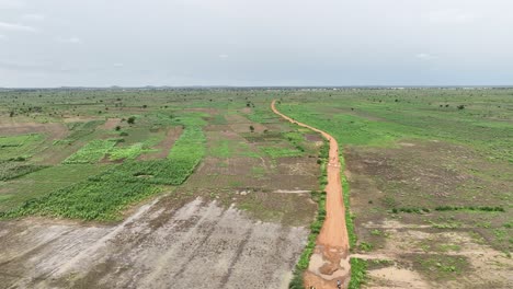 Aerial-backward-drone-shot-of-dirt-road-cutting-through-farmland-in-Africa