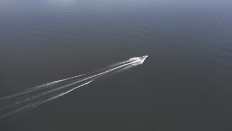 Aerial-drone-view-of-a-small-boat-going-in-the-middle-of-a-big-lake-with-people-sitting-on-it-and-behind-the-boat-there-are-a-lot-of-giants-and-a-big-huge-sea-is-visible