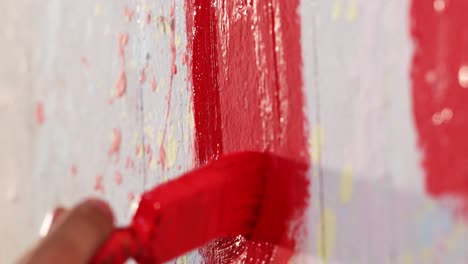 A-man-is-painting-a-wall-in-red-color-with-brush,-close-up-shot,-insert-shot