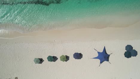 Turquoise-waters-meeting-white-sandy-beach-with-colorful-umbrellas,-aerial-view