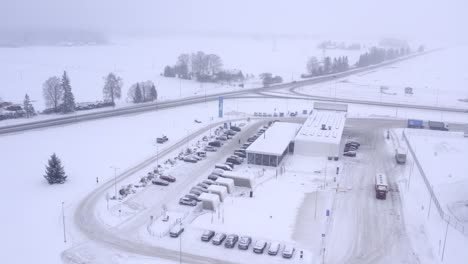 Drone-flying-over-Alexela-gas-station-and-Tikupoiss-restaurant-in-snowy-winter-weather,-at-end-we-can-see-Maxima-truck-delivering-goods