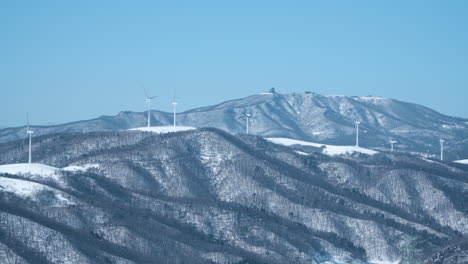 Wind-turbine-farm-on-snow-capped-mountain-range-peaks-spinning-at-Daegwallyeong-Sky-Ranch,-South-Korea