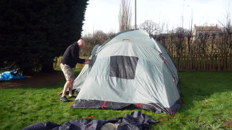 A-man-pitching-a-tent-and-attaching-poles-at-a-campsite-in-the-countryside