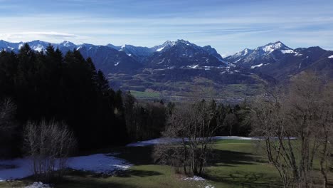 Drone-fly-between-two-small-huts-revealing-amazing-winter-mountain-landscape-with-snowcapped-mountains-and-cityscape