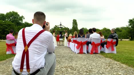 A-photographer-with-a-suspender-belt-takes-pictures-of-the-bride-and-groom-in-a-secular-ceremony,-in-a-garden-castle