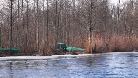 Barcos-De-Pesca-Verdes-Al-Revés-Estacionados-En-Un-árbol-Desnudo-En-La-Tranquila-Orilla-Del-Lago-Con-Ondulaciones