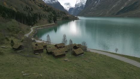 Traditional-norwegian-houses-by-the-serene-lovatnet-lake,-cloudy-day,-aerial-view