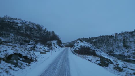 Carretera-Cubierta-De-Nieve-En-Noruega-Con-Drones-Moviéndose-Rápidamente-Hacia-Un-Automóvil-En-El-Crepúsculo