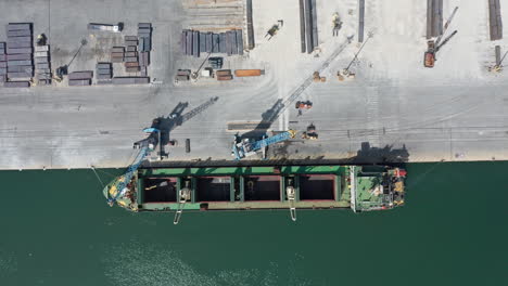 A-cargo-ship-being-loaded-at-a-busy-port-during-daylight,-aerial-view