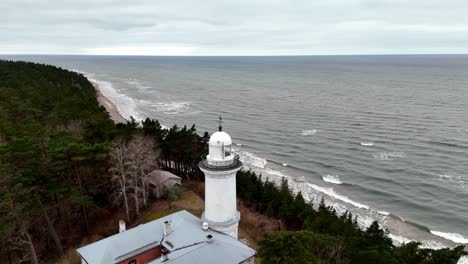A-lighthouse-in-Uzava-is-on-a-rocky-Baltic-Sea-shoreline,-large-body-of-water-in-the-background