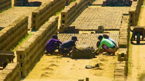 Four-young-men-squatting-on-the-ground-creating-bricks-from-raw-materials-on-a-hot-day-in-Bangladesh