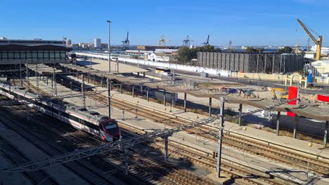 Zug-Auf-Der-Eisenbahn-Verlässt-Den-Bahnhof-Cadiz-Spanien,-Hafenkräne-Im-Hintergrund