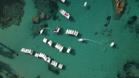 Top-down-overview-of-small-skiff-boat-turning-to-anchor-in-row-by-other-similar-marine-vessels-in-Corfu-Greece